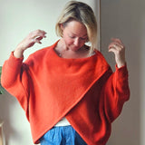 Woman wearing an orange sweater with a plant and white wall in the background
