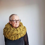 Person wearing a large yellow knitted scarf against a plain background