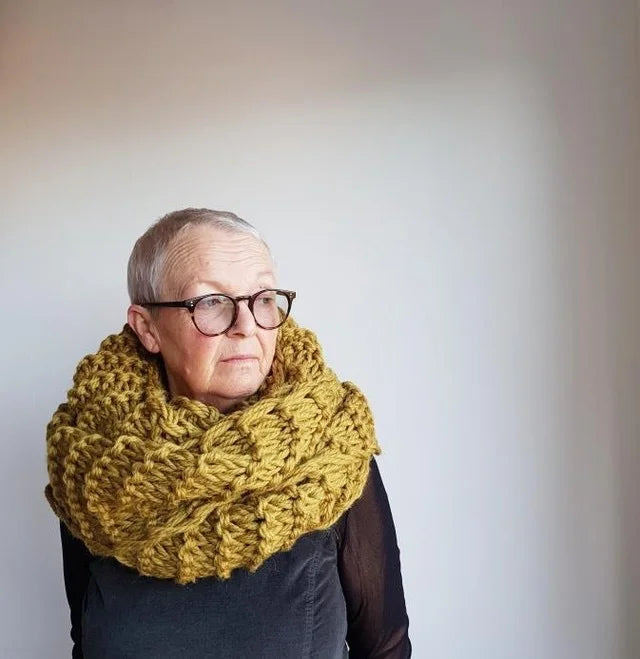Person wearing a large yellow knitted scarf against a plain background
