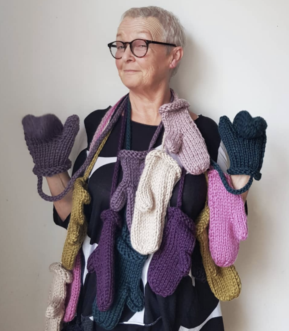 Person holding multiple pairs of colorful knitted gloves against a plain background